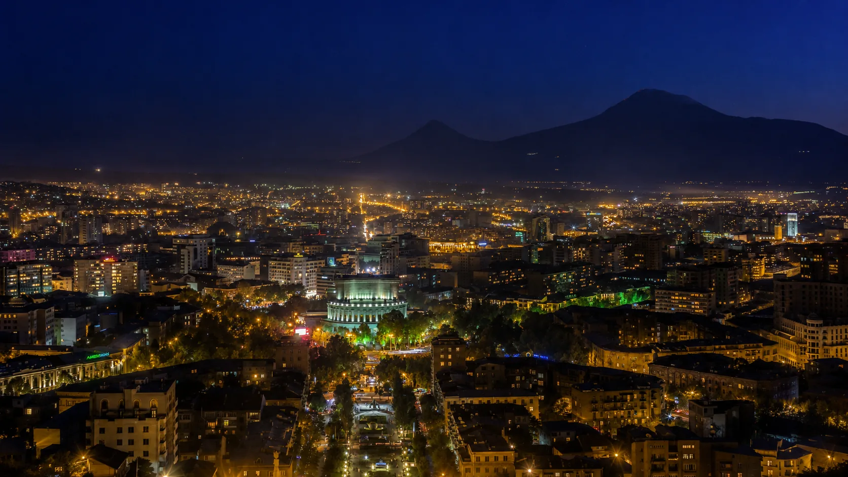 Yerevan at night, city lights spreading beneath the dark silhouette of Mount Ararat